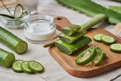 Fette di aloe vera fresche su tagliere con barattolo di crema cosmetica sullo sfondo.